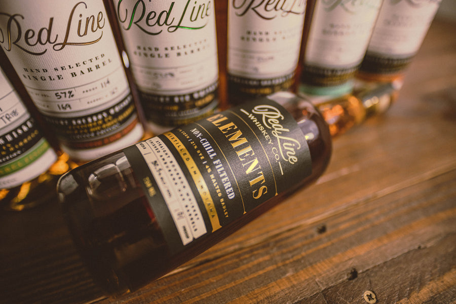 Red Line hand-selected single barrel bottles behind a bottle of Red Line Elements on a wooden table